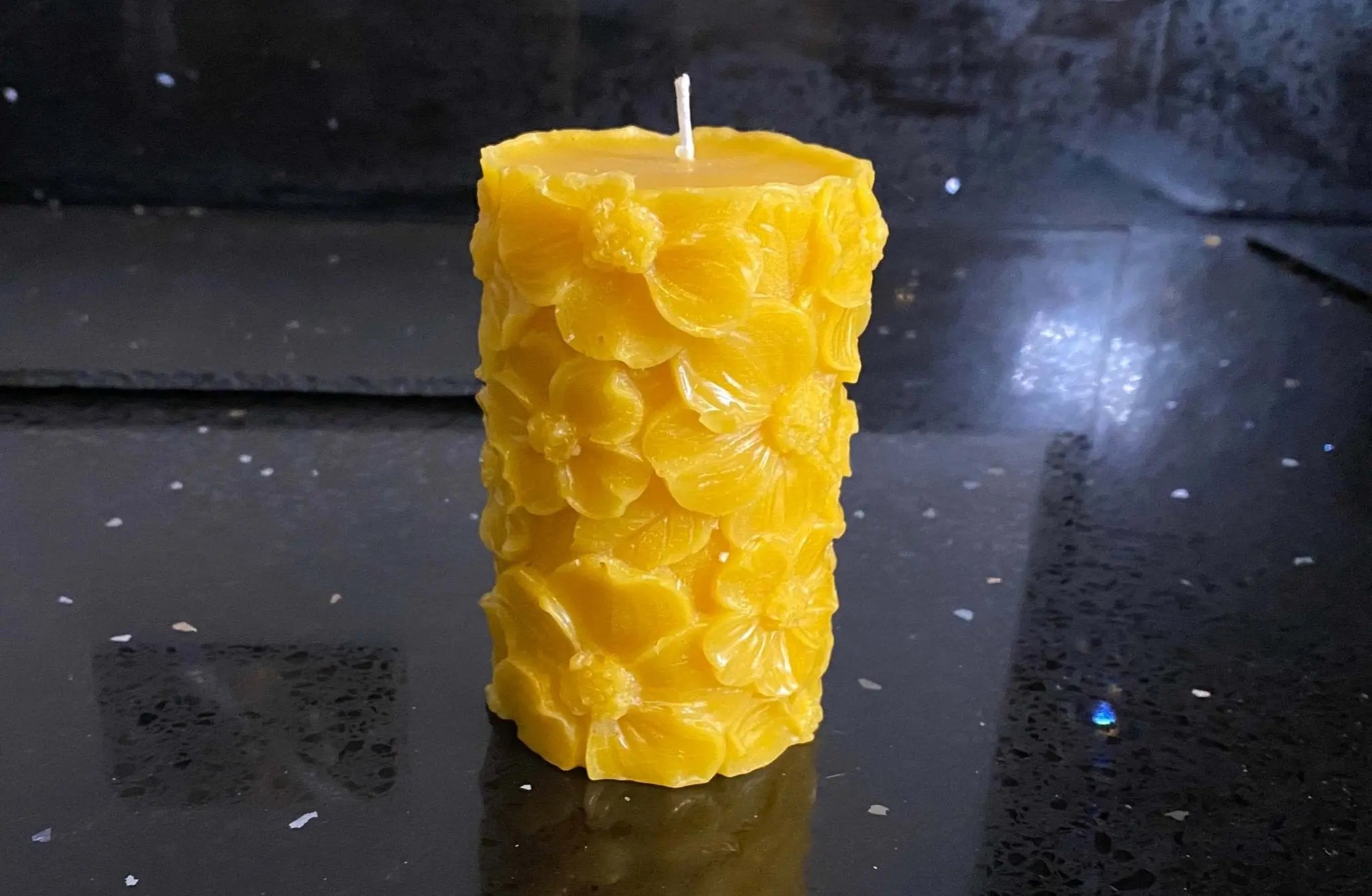 Yellow beeswax candle with embossed floral design on a dark reflective surface