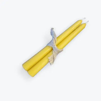 Pair of handmade yellow beeswax taper candles tied with decorative ribbon on white background