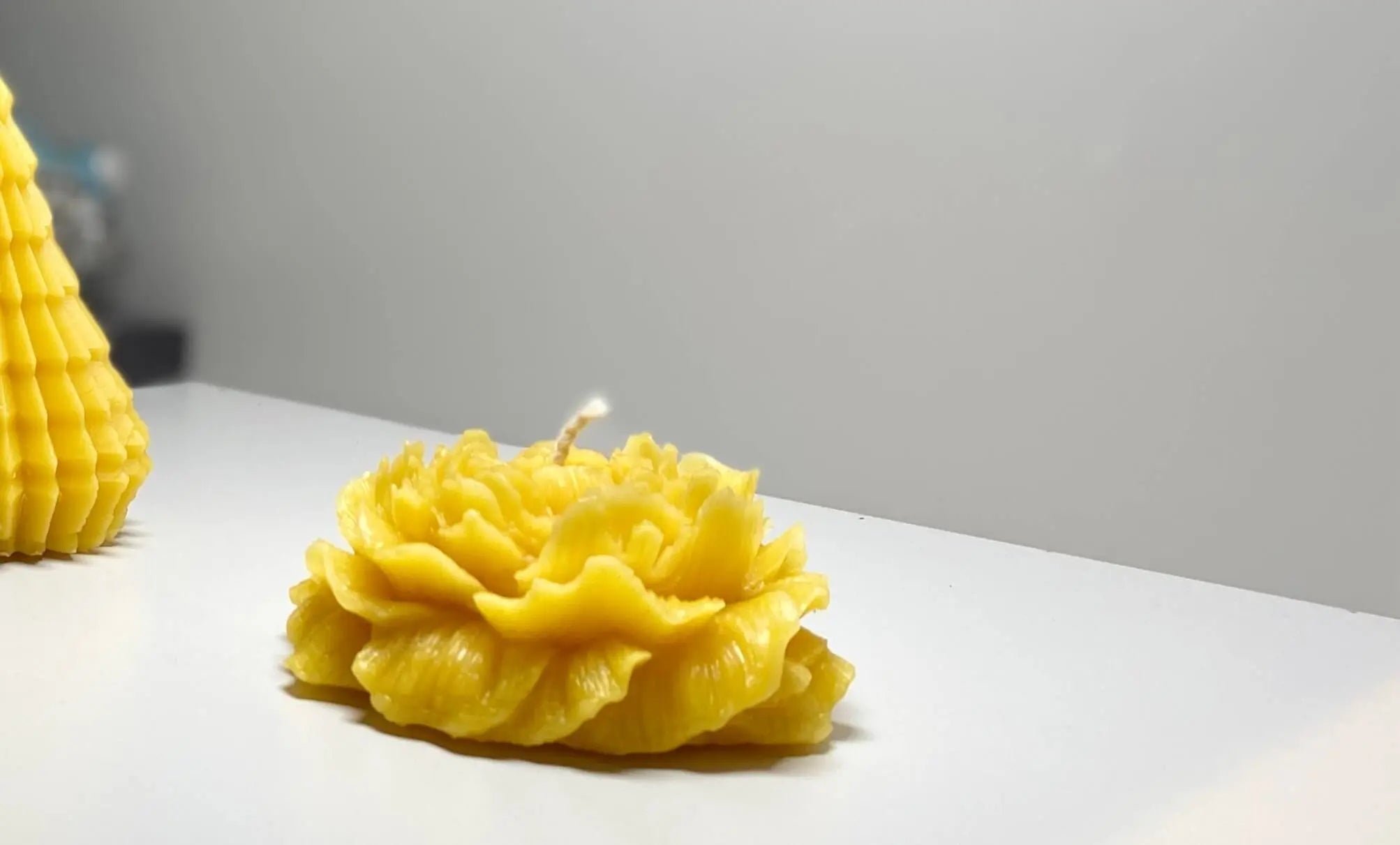 Handmade natural yellow beeswax candle shaped like a rose on a white surface