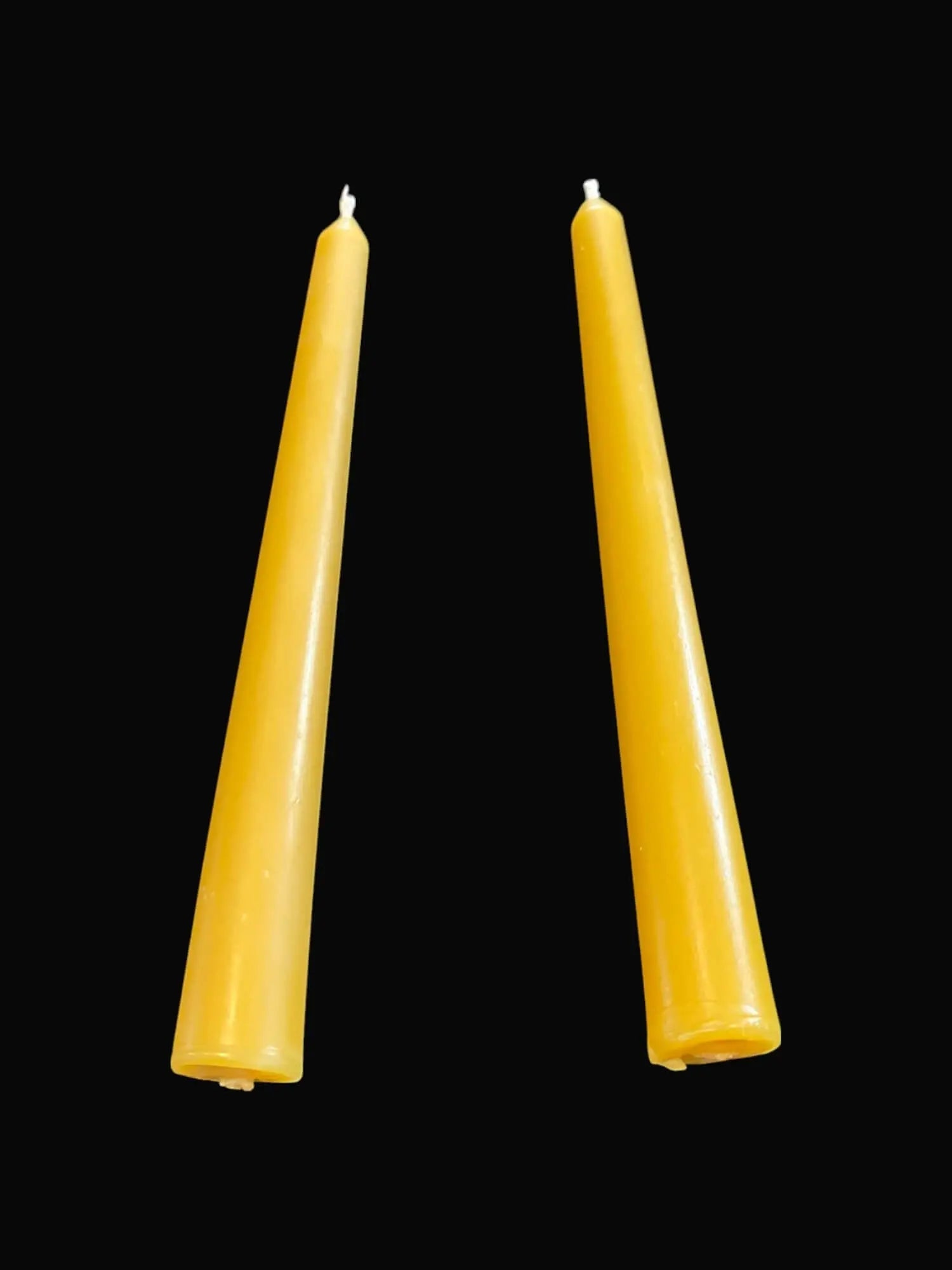 Pair of handmade yellow beeswax taper candles on black background
